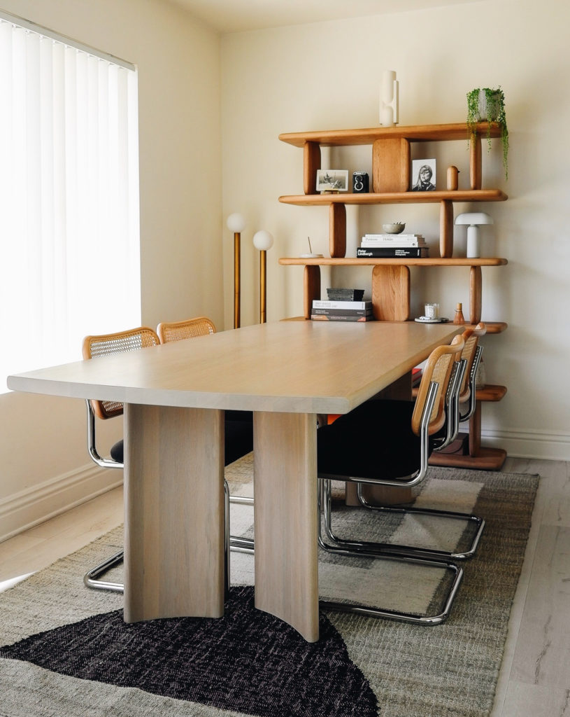 Lulu and Georgia Furniture review: A modern and minimal dining room with handmade flatweave natural, geometric rug, curved and minimal solid wood dining table, organic and sculptural wooden bookcase, and a playful accent floor lamp.